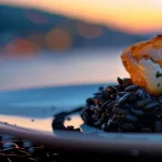 Croatian crni rizot, squid ink risotto, deep black contrasting with a white plate, seaside restaurant, dusk lighting reflecting off the water